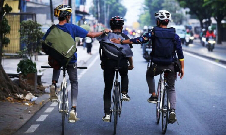  Tiga orang kurir mengayuh sepeda sambil membawa tas dan mengenakan helm